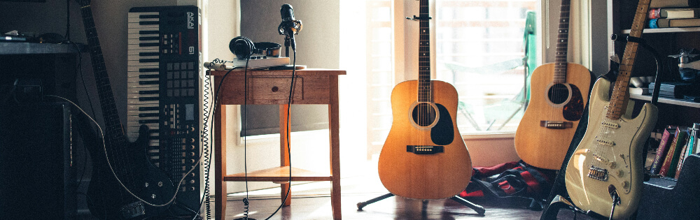 Raum mit Musikinstrumenten, darunter ein Keyboard, ein Tisch mit Kopfhrern und einem Mikrofon, zwei Akustikgitarren und eine E-Gitarre.